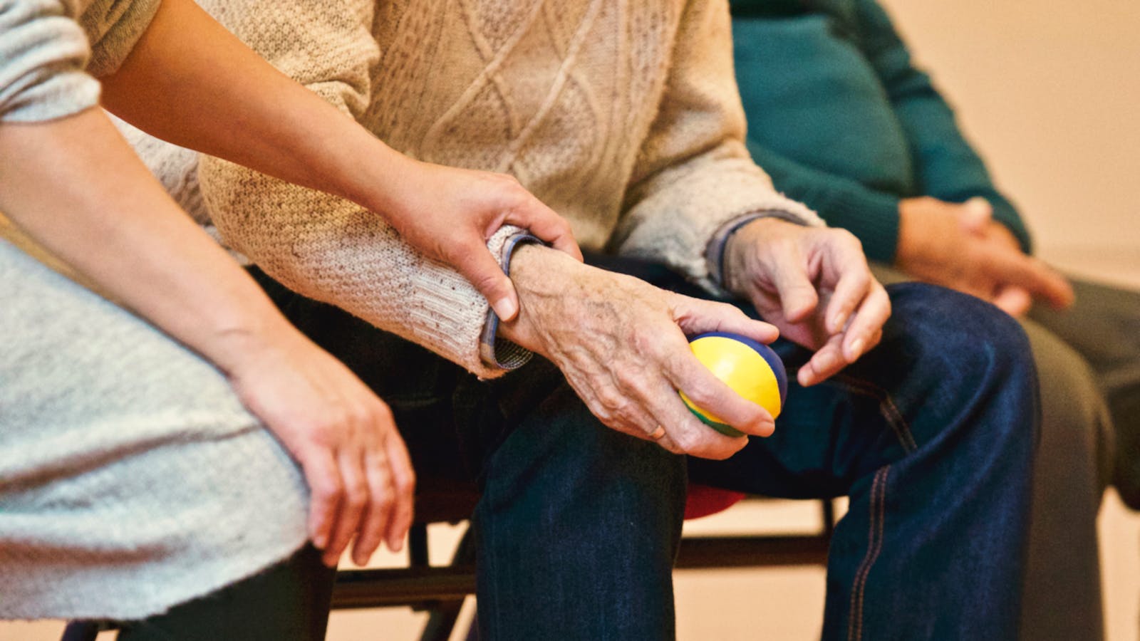 An elderly person receives support from a caregiver, holding hands indoors, showcasing compassion.